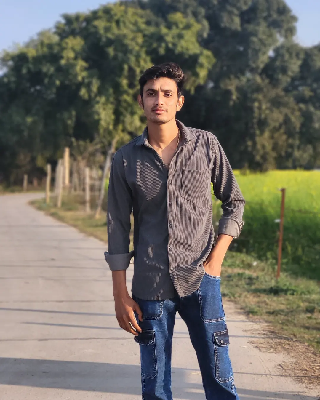 A person in a dark shirt standing on a sunlit path beside green fields